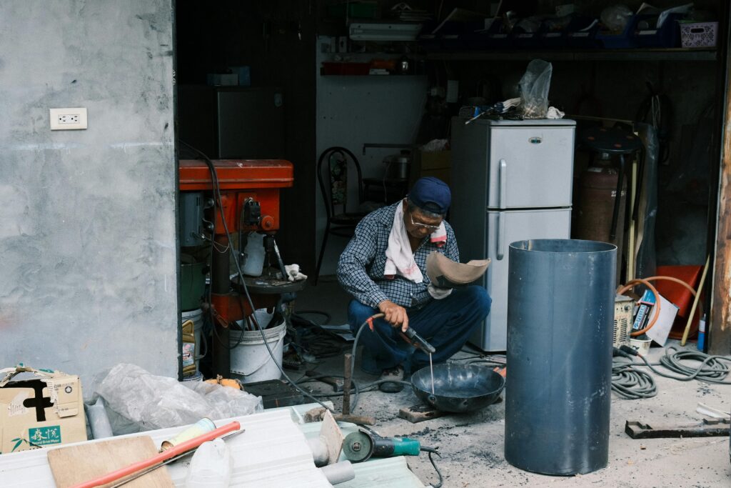 An adult man welding in a garage in Taiwan, surrounded by tools and equipment.