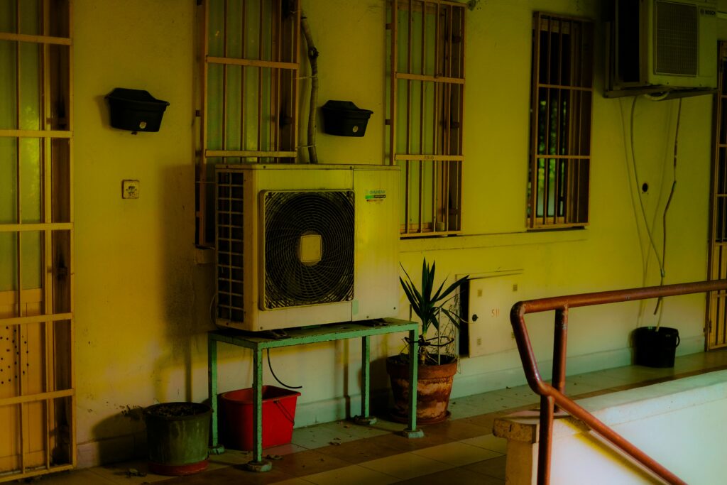 Outdoor air conditioning unit on a balcony with potted plants and building features, offering urban vibes.
