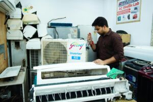 Technician repairing an air conditioner unit in New Delhi workshop.